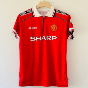 Red Manchester United retro home jersey featuring a white, black, and red collar, Umbro logos on the shoulders, and the white SHARP sponsor logo across the chest.