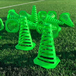 Set of bright fluorescent green, stacked, and slotted/vented soccer training cones scattered on a turf field, used for agility drills and marking boundaries.